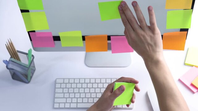 Man putting sticky notes onto computer at white table, above view. Multitasking and deadline