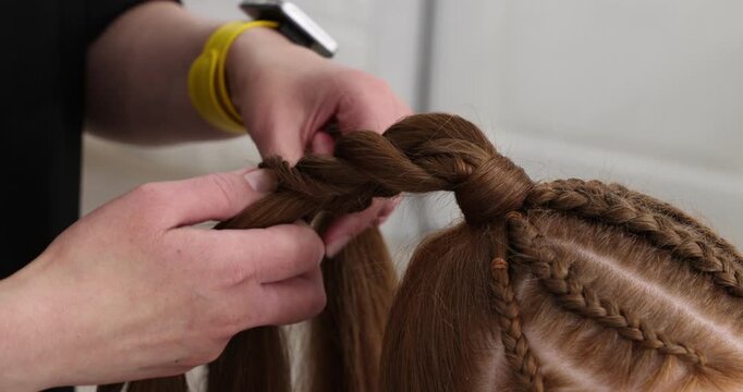 Hairstylist braiding teenage girl's hair in salon, closeup. Camera moving