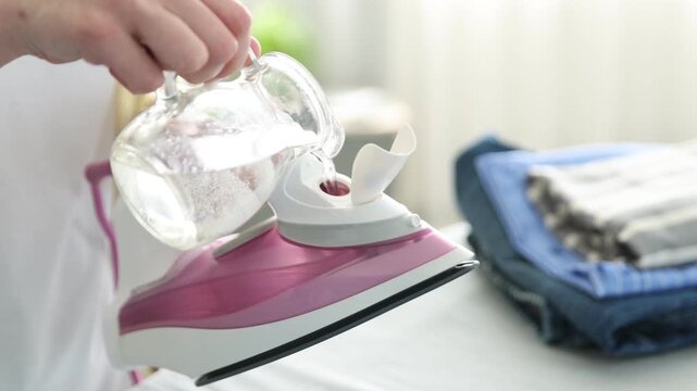 Woman pouring water into modern iron near ironing board at home, closeup
