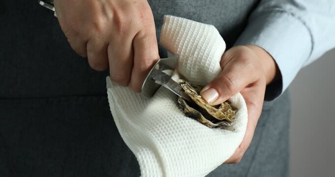 Woman opening oyster with knife on grey background, closeup