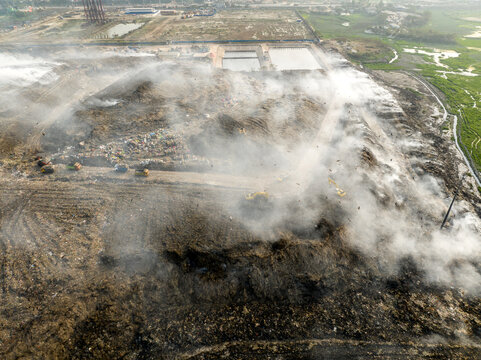 Aminbazar, Bangladesh - 21 February 2026: Aerial view of the Aminbazar landfill with smoke rising from garbage piles and excavators working on the site.