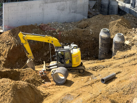 View of a yellow excavator working at a construction site with concrete pipes and dirt mounds in Avcilar, Istanbul, Turkiye.
