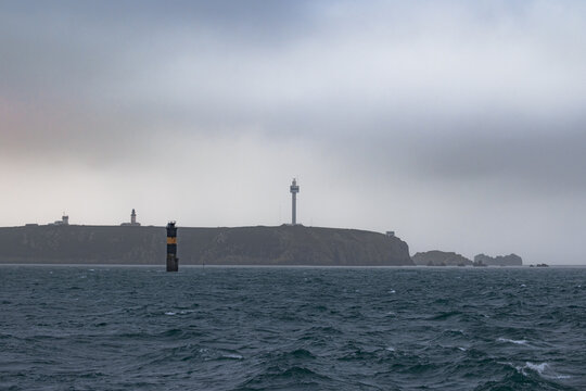 View of the Phare du Stiff lighthouse and radar tower standing on the rugged cliffs of the island under an overcast sky Ushant, Brittany, France.