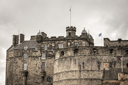 View of the historic Edinburgh Castle with its ancient stone battlements and flags under an overcast sky in Edinburgh, Scotland, United Kingdom.