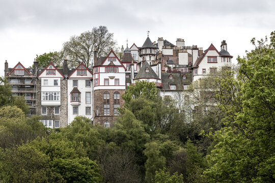 View of the historic Ramsay Garden buildings with white facades and red timber framing nestled among lush green trees in Edinburgh, Scotland, United Kingdom.