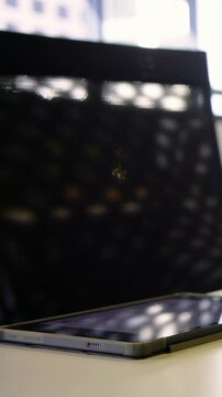 Vertical video: Shifting focus camera revealing cased phone on desk by window, showing mesh chair