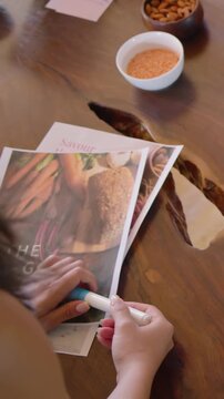Vertical video: Reaching hands rolling tool across recipe pages at home to smooth pages, with watch