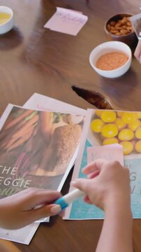 Vertical video: Reaching hands lifting 'VEGGIE BOWL' cover at dining table, binding recipe covers