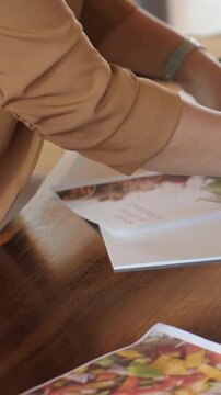 Vertical video: Preparing booklets, woman in tan top aligning as hand reaching at table with fruit