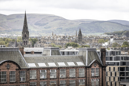 View of historic rooftops, church spires, and rolling hills under an overcast sky in Edinburgh, Scotland, United Kingdom.