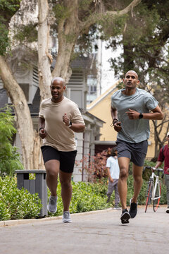 African American men jogging together on tree-lined residential path wearing watches, running shoes