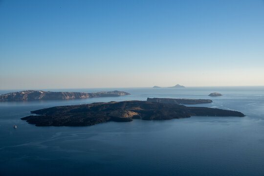 View of the volcanic islands of Nea Kameni and Palea Kameni in the Santorini caldera under a clear blue sky in Fira, Greece.