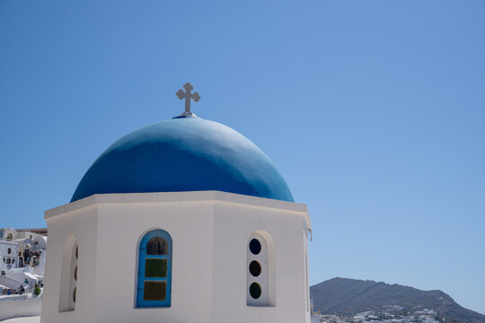 View of the Three Bells of Fira blue-domed church with white walls under a clear blue sky in Fira, Greece.