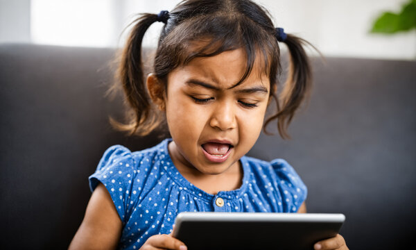 young kid sitting comfortably on a couch holding a tablet complaining and whining about a difficult online problem causing emotional stress