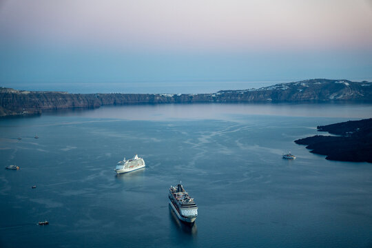 View of cruise ships anchored in the calm waters of the caldera bay surrounded by steep volcanic cliffs under a soft twilight sky Fira, Greece.