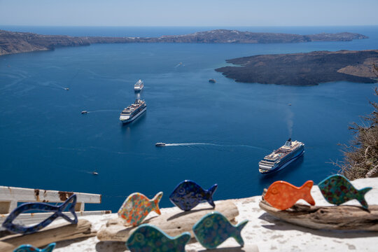 View of cruise ships anchored in the blue waters of the caldera with colorful ceramic fish decorations in the foreground in Fira, Greece.
