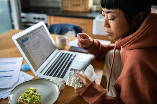 Sick woman taking medicine while working from home in kitchen