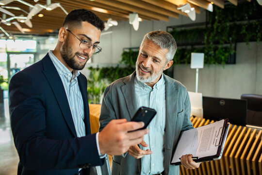 Coworkers discussing smartphone in modern office lobby
