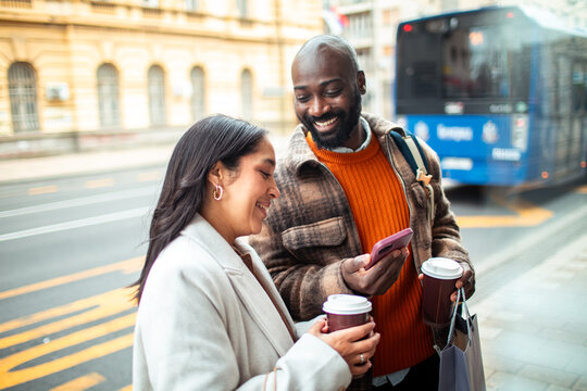 Smiling friends with coffee using smartphone at city bus stop