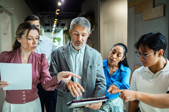 Diverse business team discussing project with tablet in office hallway