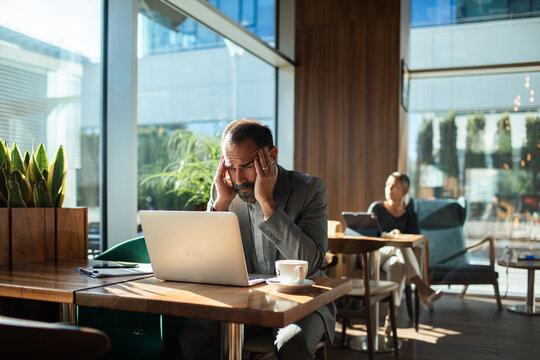 Stressed businessman with headache working on laptop in cafe