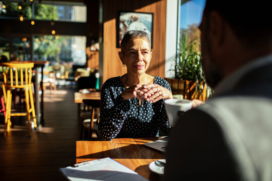 Senior woman meeting with colleague in sunlit cafe