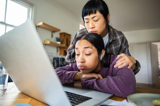 Parent comforting stressed teen over homework on laptop at kitchen table