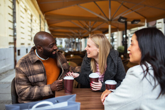 Friends laughing over coffee at outdoor city cafe