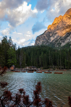 View of Pragser Wildsee with wooden rowing boats near a boathouse surrounded by a pine forest and towering Dolomite mountains at sunset in Prags, Trentino-Alto Adige, Italy.