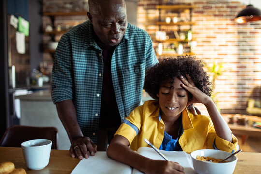 Parent helping child with homework at kitchen table at home