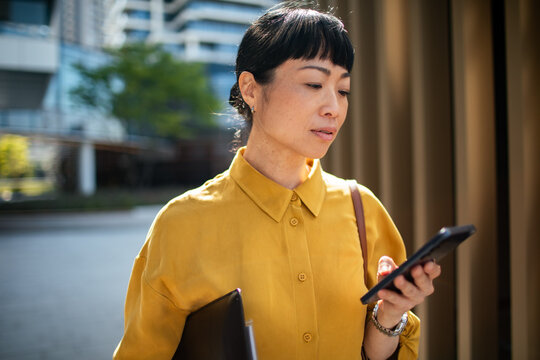 Businesswoman checking smartphone outside modern office building