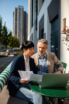 Two business colleagues reviewing documents at outdoor cafe in city