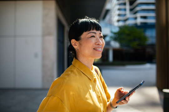 Smiling woman using smartphone outdoors in modern city