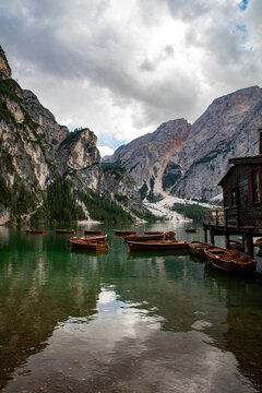 View of Pragser Wildsee with wooden rowing boats on the water and a rustic boathouse against the backdrop of the Dolomites mountains in Prags, Trentino-Alto Adige S, Italy.