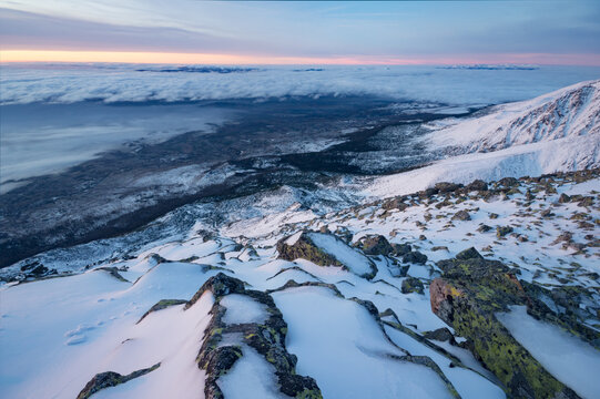 View of the snow-covered rocky slopes of Slavkovsky stit overlooking a sea of clouds in the valley at sunset Vysoke Tatry, Presovsky kraj, Slovakia.