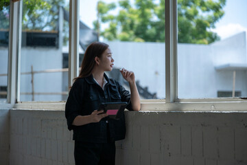 Fototapeta premium Thoughtful woman with tablet gazing out a window in modern space