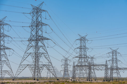 View of high-voltage power lines and transmission towers stretching across a desert landscape under a clear blue sky UAE.