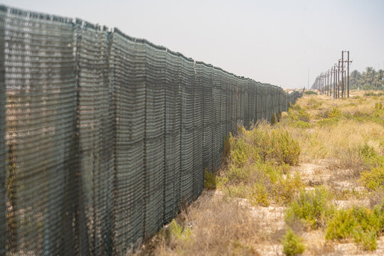 View of a long metal mesh fence stretching across a dry scrubland with utility poles under a clear sky in UAE.