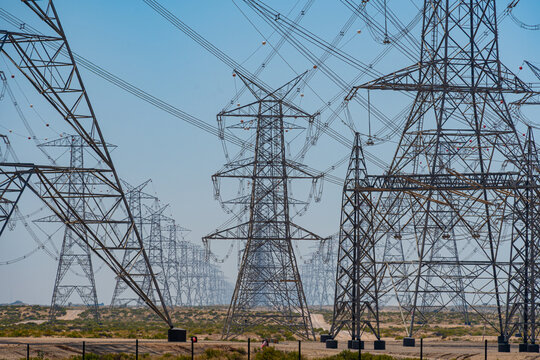 View of high-voltage electricity pylons and power lines stretching across an arid desert landscape under a clear blue sky UAE.