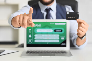 Fototapeta premium Young businessman with credit card and laptop using virtual screen at office, closeup. Online banking concept
