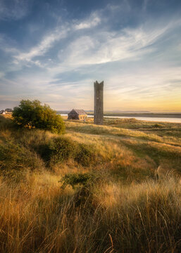 View of Maiden Tower standing in a grassy field near the Boyne estuary with a stone building and wispy clouds at sunset in County Meath, Ireland.