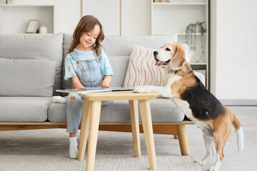 Naklejka premium Cute little girl with Beagle dog reading book at table in living room
