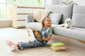 Naklejka premium Cute little happy girl with Maltese dog and books reading on floor at home