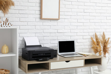 Modern printer with laptop on table near white brick wall in home office