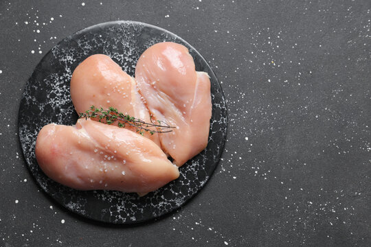 Board with raw chicken breast and thyme on black background