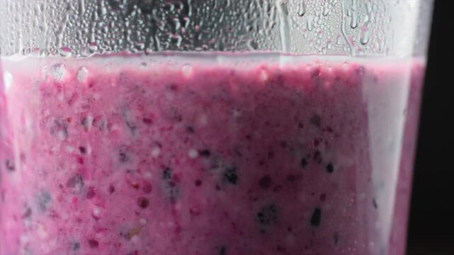 berry smoothie pouring into glass close-up, thick purple mixture flowing and rising inside transparent glass with visible seeds and droplets, healthy drink concept, freshness and nutrition