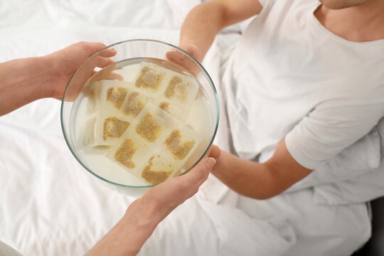Young woman bringing bowl of water with mustard plasters to her sick husband in bedroom, closeup