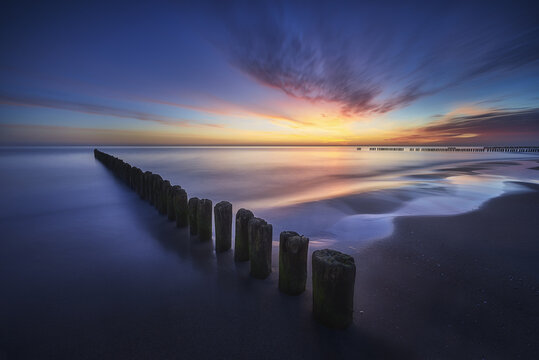 View of wooden breakwater groynes on a sandy beach during a colorful sunset over the Baltic Sea Chalupy, Wojewodztwo pomorskie, Poland.