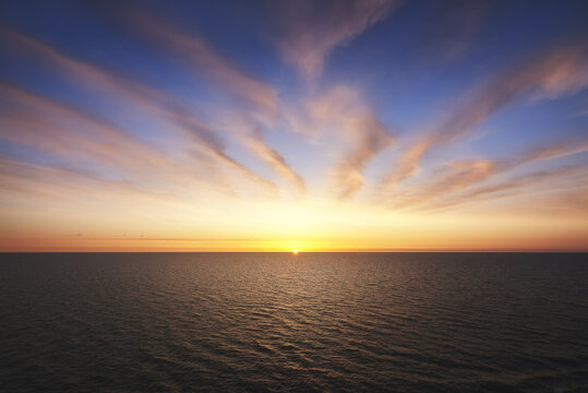 View of the sun setting on the horizon of the Baltic Sea with dramatic radiating clouds in the colorful sky in Sweden.