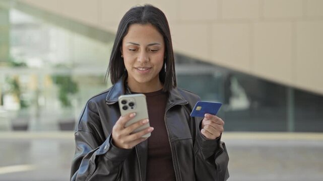 Woman holding smartphone and creditcard, hand raised and tapping phone while smiling with eyes closed in building; happiness convenience.